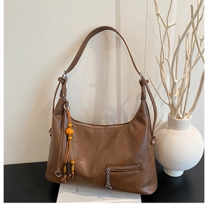 Détail d'un sac cabas marron foncé avec pompon ethnique et breloque trèfle en métal