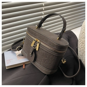 Detail of a brown bucket box bag with crocodile pattern and contrast stitching on dark fabric