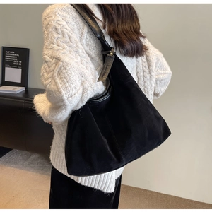 Detail of a large black suede hobo shoulder bag styled with a white cable knit sweater