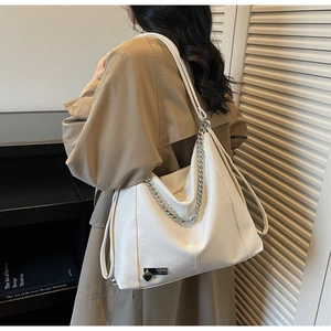 Detail of white faux leather tote bag with silver chain strap and heart pendant accessory