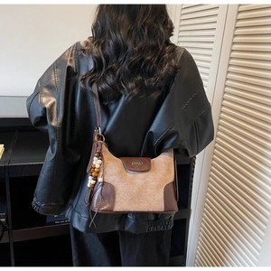 Side view of faux suede dumpling bag with leather trim and ethnic bead charm on strap