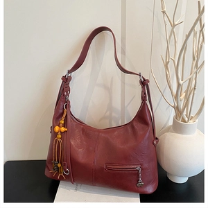 Détail du sac cabas bordeaux avec breloque à pompon et fermeture éclair trèfle en métal