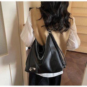 Detail of black faux leather tote bag featuring chunky silver chain and heart charm pendant