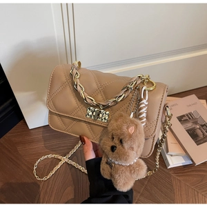 Close-up of quilted leather crossbody bag with golden twist lock and plush bear charm