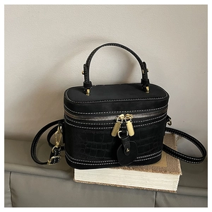 Detail of black box bag with crocodile texture, white stitching and gold metal hardware