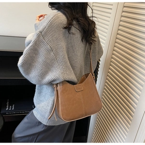 Close-up of brown leather half-moon shoulder bag with sleek stitching and logo plate