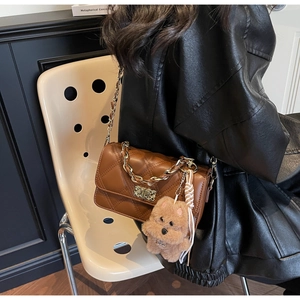 Close-up of brown quilted crossbody bag with gold chain and plush teddy bear charm