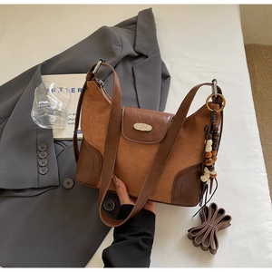 Detail view of brown patchwork dumpling bag with suede texture and decorative tassel charm