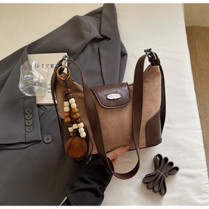 Detail view of brown leather crossbody bag with wooden bead charm and extra shoulder strap
