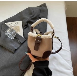Détail d'un sac seau en peluche beige avec bordures en cuir marron et boucle dorée chic