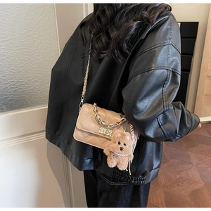 Detail of light brown quilted crossbody bag with gold chain strap and cute bear charm