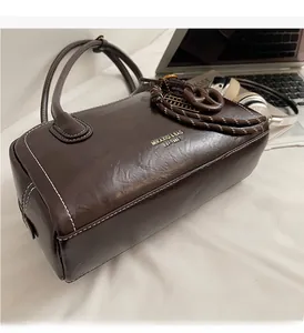Détail du sac Boston marron foncé avec logo doré, surpiqûres et poignée en nœud tressé