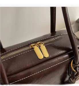 Gros plan détaillé des doubles fermetures éclair dorées sur un sac en cuir ciré marron foncé