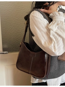 Retro dark brown leather bucket bag with wide strap worn by a model in a casual outfit