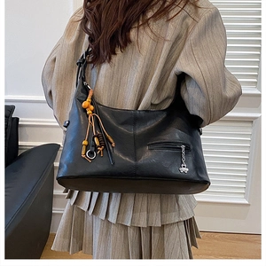Détail du sac hobo en cuir noir avec pompon en perles de bois et pendentif trèfle