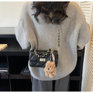 Detail of quilted crossbody bag with gold chain strap and plush puppy charm