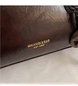 Gros plan du sac à main vintage en cuir marron avec logo doré métallique et texture premium