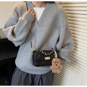 Detail of a black quilted chain shoulder bag with a cute plush charm on a grey sweater