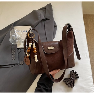 Detail of dark brown dumpling bag with suede patchwork and beaded charm on gray blazer
