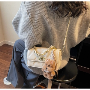 Detail of cream quilted chain bag featuring gold twist lock and plush puppy charm