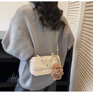 Close-up of cream quilted crossbody bag with gold chain and a cute plush dog charm