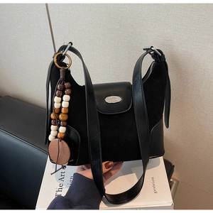Detail of black suede hobo bag with silver buckle and decorative wooden bead tassel