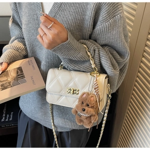 Detailed close-up of white quilted crossbody bag with gold hardware and a teddy bear charm