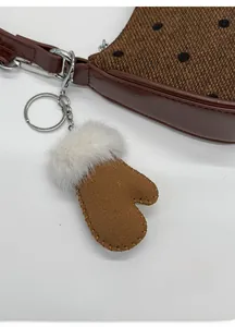 Detailed close-up of brown suede glove charm with white faux fur trim on shoulder bag