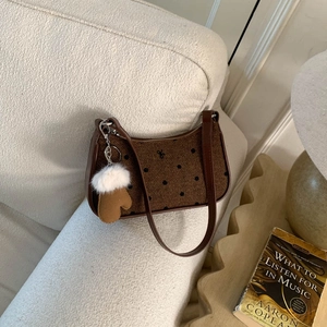 Close-up of polka dot underarm bag with plush glove charm on a textured sofa