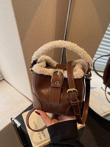 Sac seau en cuir marron avec bordure en polaire et boucle dorée dans un décor chaud