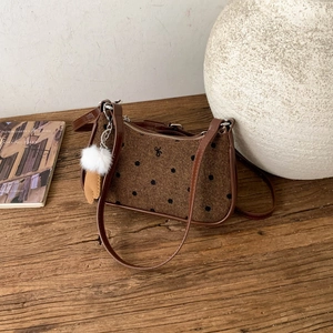 Detail of a brown polka dot underarm bag with plush charm on a wooden texture background
