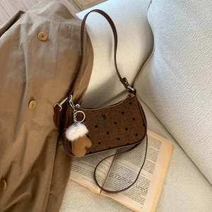 Close-up of brown polka dot underarm bag with a plush glove charm on a cozy sofa