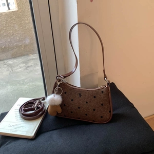 Close-up of brown polka dot wool baguette bag featuring a cute plush glove charm and leather strap