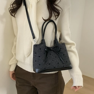 Close-up of a grey polka dot tote bag with leather bow detail on white knitwear background