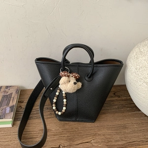 Close-up of black lychee texture tote bag with plush bear charm and beaded handle
