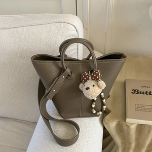Close-up of brown pebbled leather bucket bag with cute bear charm on a soft sofa
