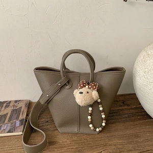 Detail of taupe pebbled leather bucket bag with cute plush bear charm and beaded strap
