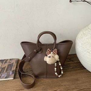 Detail of a brown lychee pattern bucket bag with a cute plush bear charm decoration