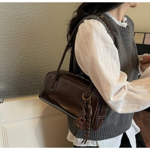 Détail d'un sac Boston en cuir marron foncé avec coutures blanches et longue bandoulière