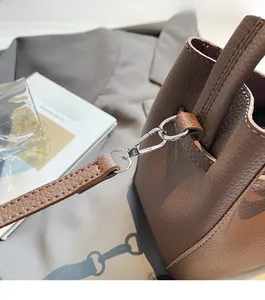 Detailed close-up of silver metal hardware and stitching on brown litchi leather bag