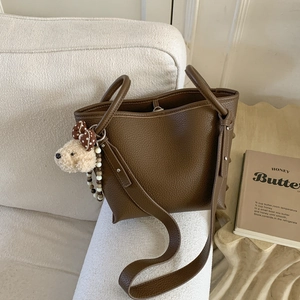 Brown litchi leather tote bag with plush bear charm on a cozy cream textured sofa