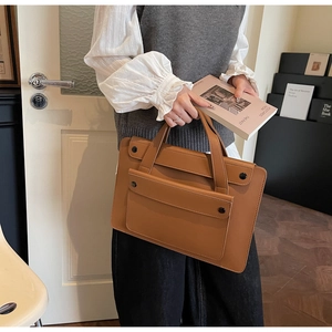 Detail of a brown leather laptop bag with an envelope pocket and reinforced handle