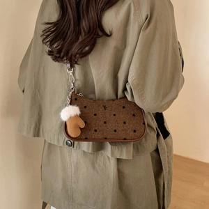 Close-up of brown polka dot shoulder bag with leather strap and plush glove charm