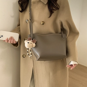 Detail shot of a taupe bucket bag with a cute bear charm and adjustable shoulder strap