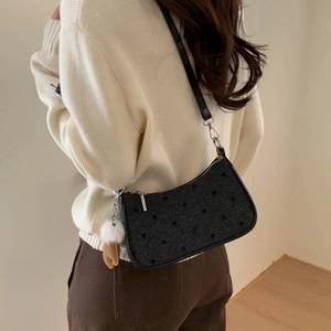 Detail of black polka dot underarm bag with fuzzy charm worn by a model