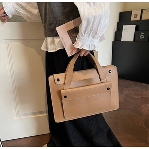 Close-up of matte tan leather briefcase featuring a minimalist pocket and round snap button