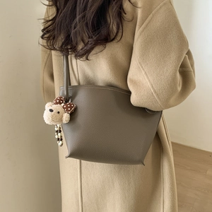 Detail of dark brown pebble leather tote bag with cute bear pendant on a wool coat