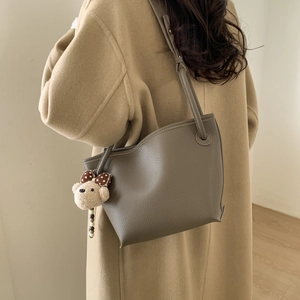 Detailed view of grey pebble leather bucket bag with cute bear charm worn on the shoulder