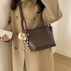 Close-up of brown litchi pattern leather bucket bag with cute bear charm on khaki coat