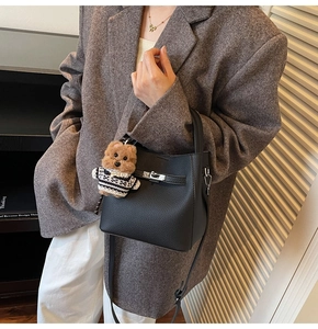 Detail of black pebbled leather bucket bag with silver lock and teddy bear charm accessory